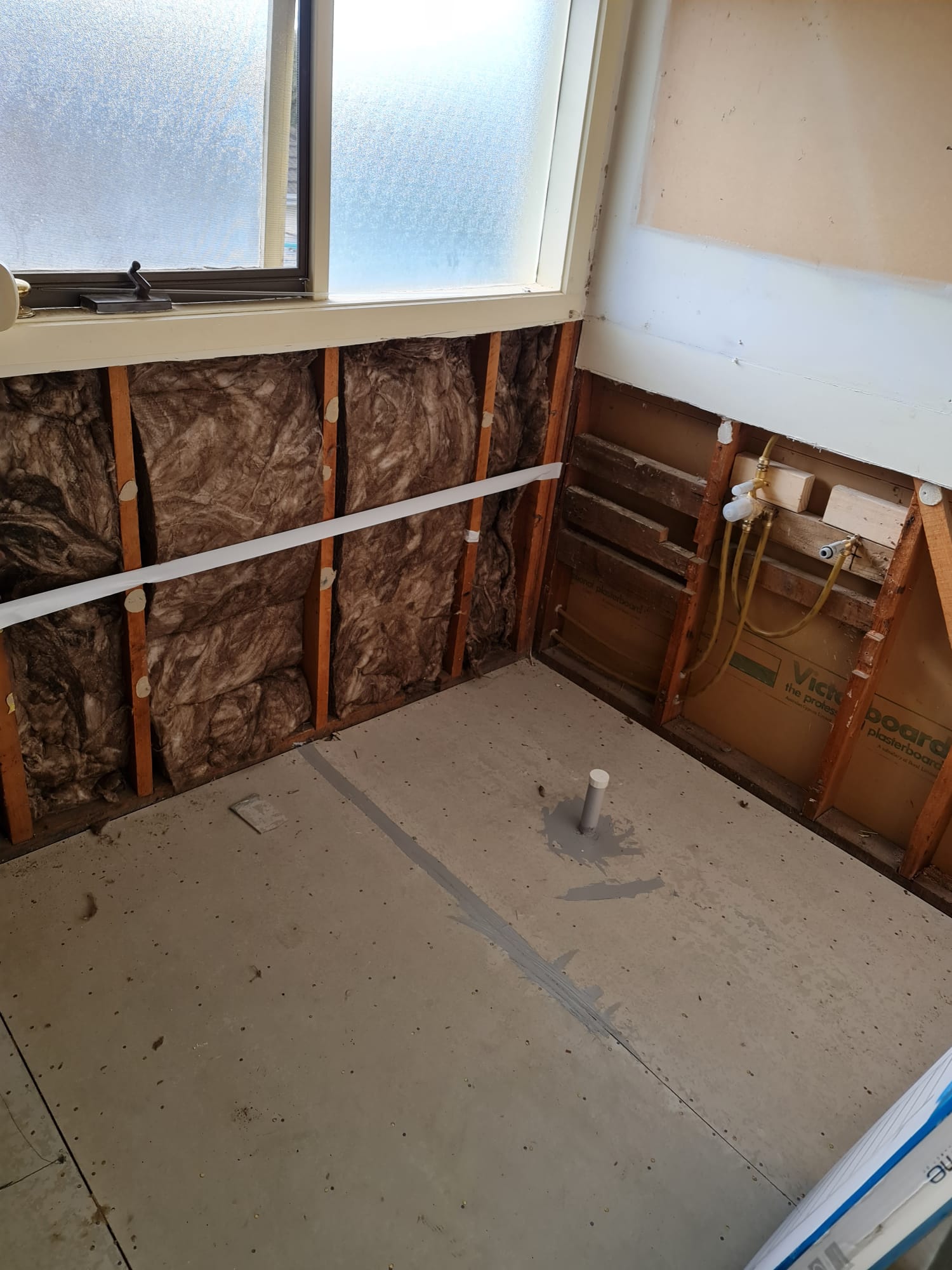 Exposed insulation batts and old plumbing during bathroom strip-out