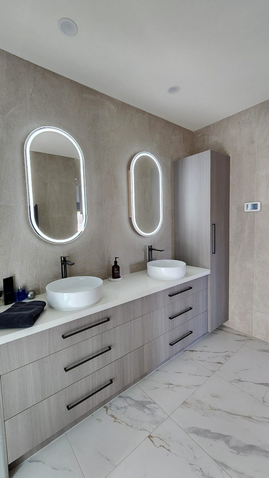 Double floating vanity with twin white vessel basins, matte black tapware and LED oval mirrors