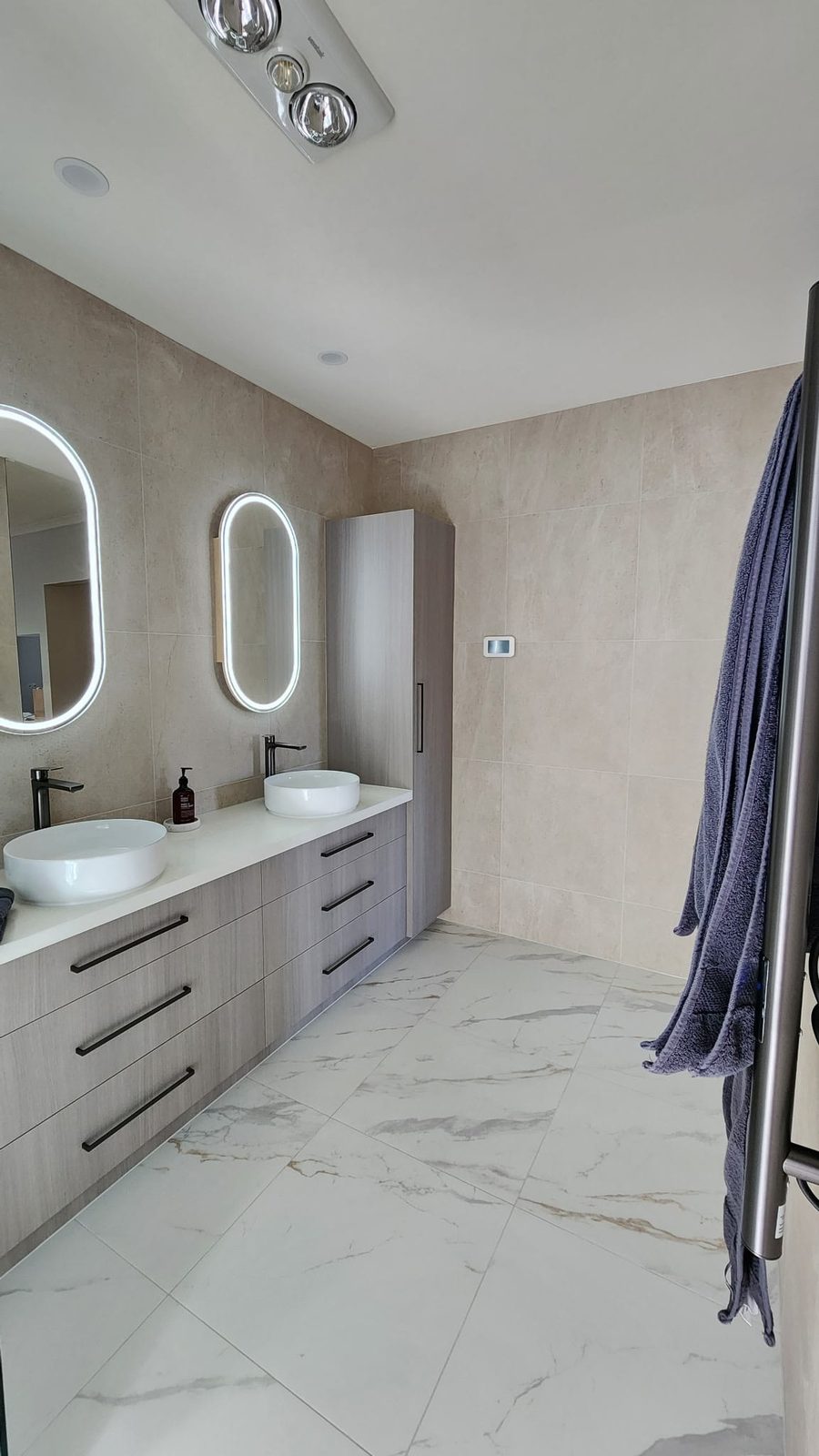 Full-height storage tower beside the double vanity in a warm neutral bathroom