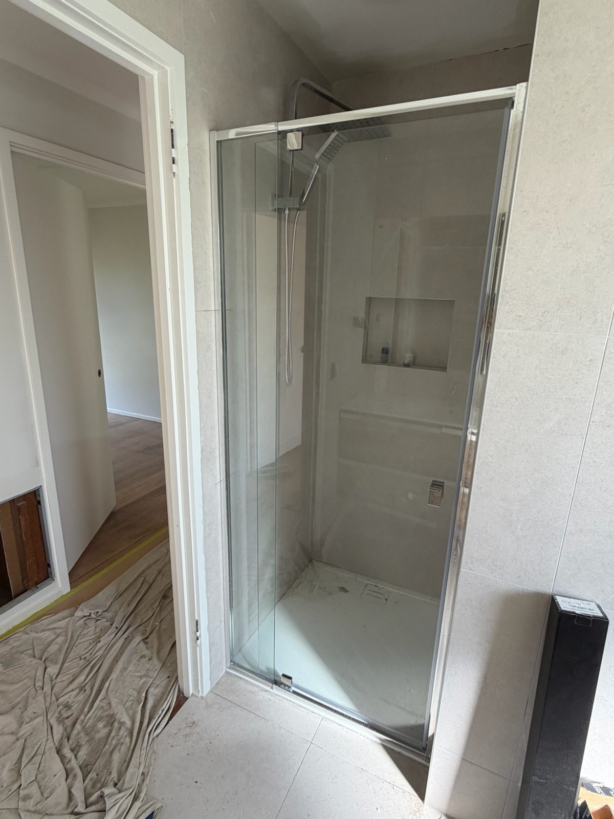 Belmont bathroom renovation in progress — large light grey wall tiles in the shower zone, chrome-framed glass shower enclosure and recessed niche