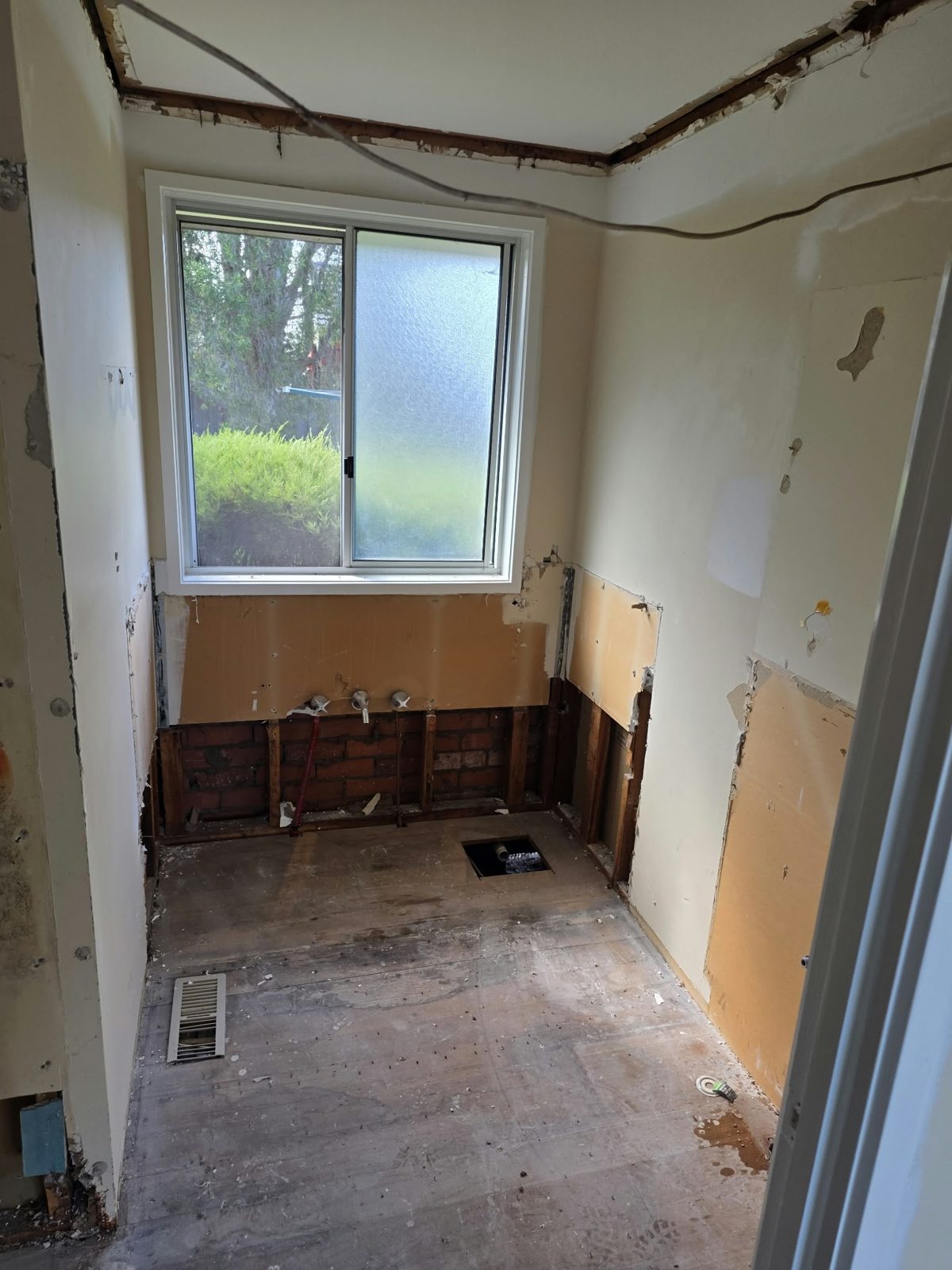 Belmont bathroom stripped back to bare walls — existing plumbing rough-in visible below the window