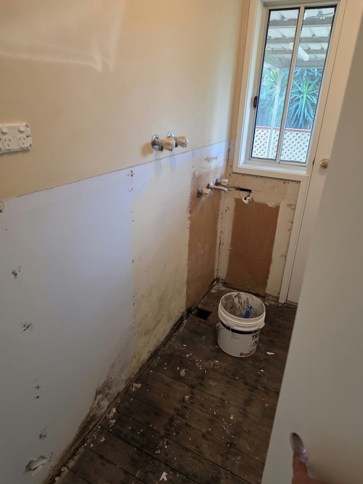 Belmont bathroom strip-out — wall cladding removed, original shower taps still in place, bare timber floorboards visible