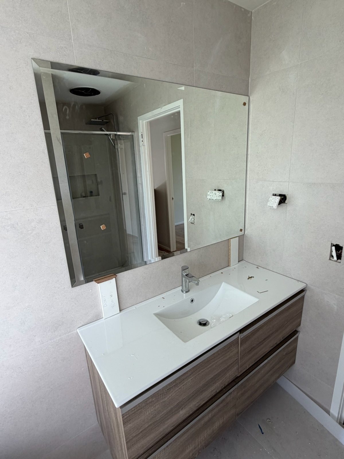 Belmont bathroom renovation by Ultimate Renovations — wall-hung timber-look vanity, white integrated basin, chrome tap and large rectangular mirror against light grey tiles
