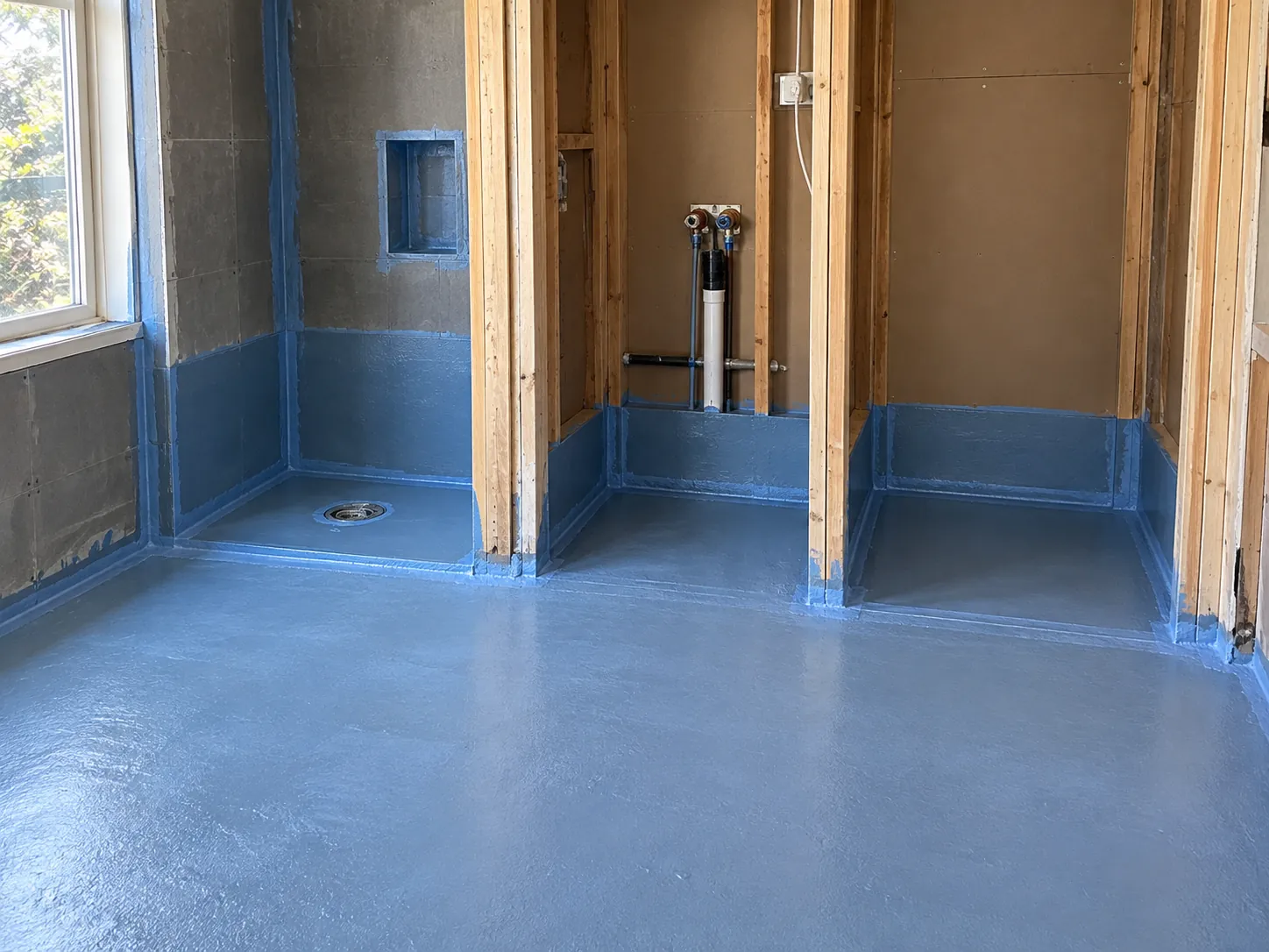 A combined bathroom and laundry floor mid-renovation showing full waterproofing membrane across both the shower and laundry zones