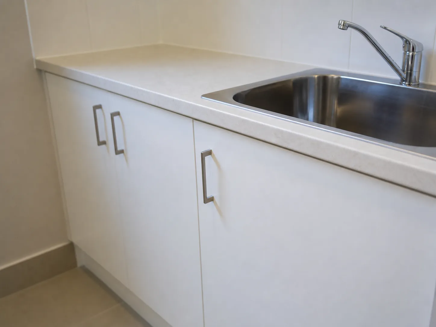 Close-up of a laundry bench with a laminate benchtop, standard-width cabinet doors and a stainless steel trough