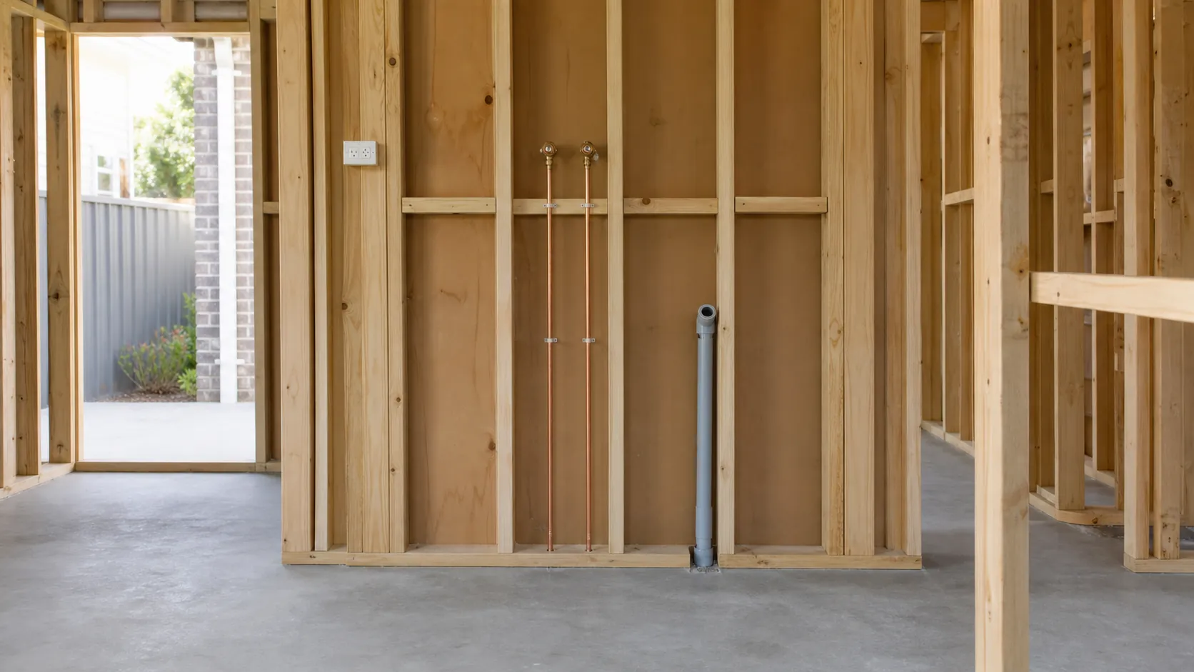 Laundry at rough-in stage with exposed wall framing, water and waste pipes and a power point before the walls are closed up