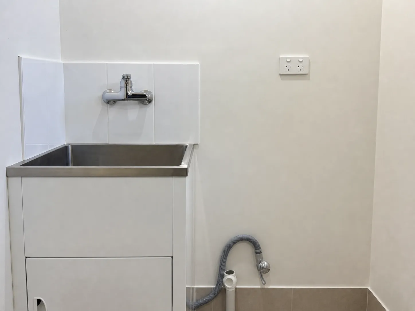 Laundry wall with a mixer tap over a stainless steel trough and a wall-mounted power point beside the washing machine space