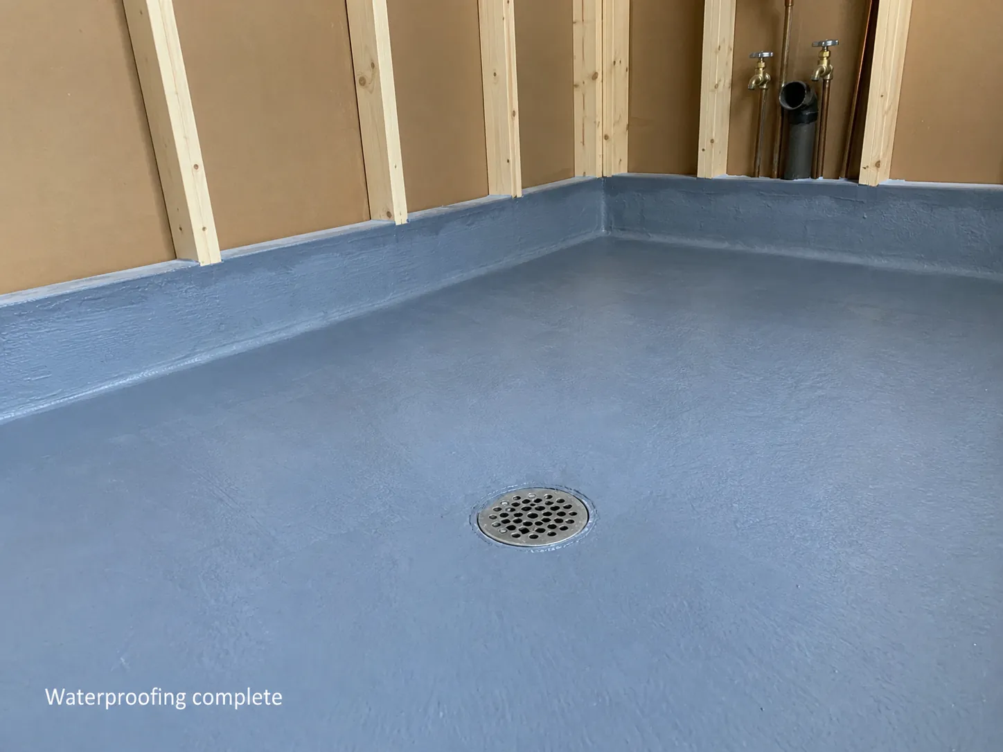 A laundry floor mid-renovation showing a waterproofing membrane and floor waste before tiling