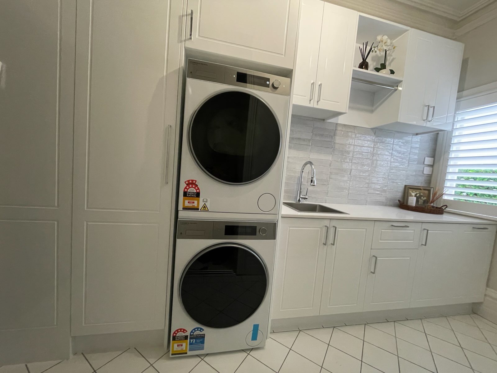 Stacked front-load washer and dryer beside full-height white shaker cabinetry — laundry renovation by Ultimate Renovations, Geelong