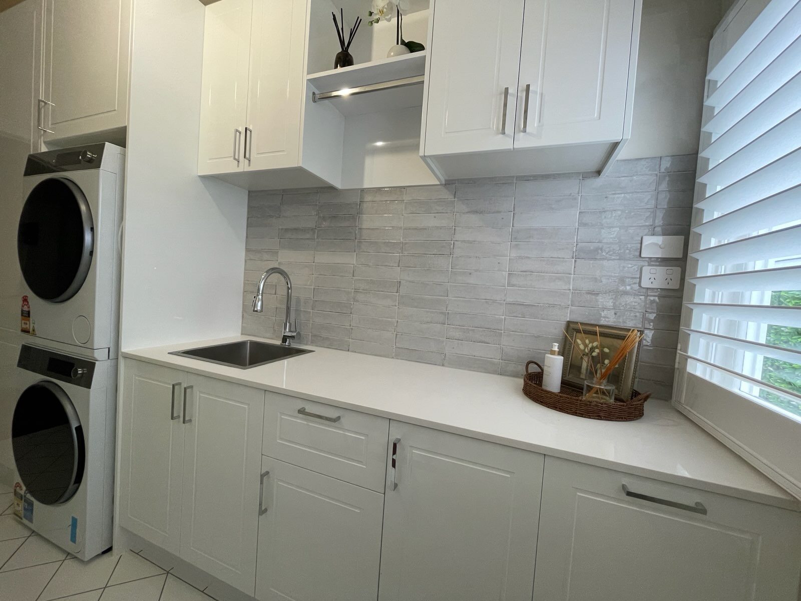Grey rectangular laundry splashback tiles above white benchtop with stainless-steel sink — splashback tiles supplied by Devine Tiles for this Geelong laundry renovation