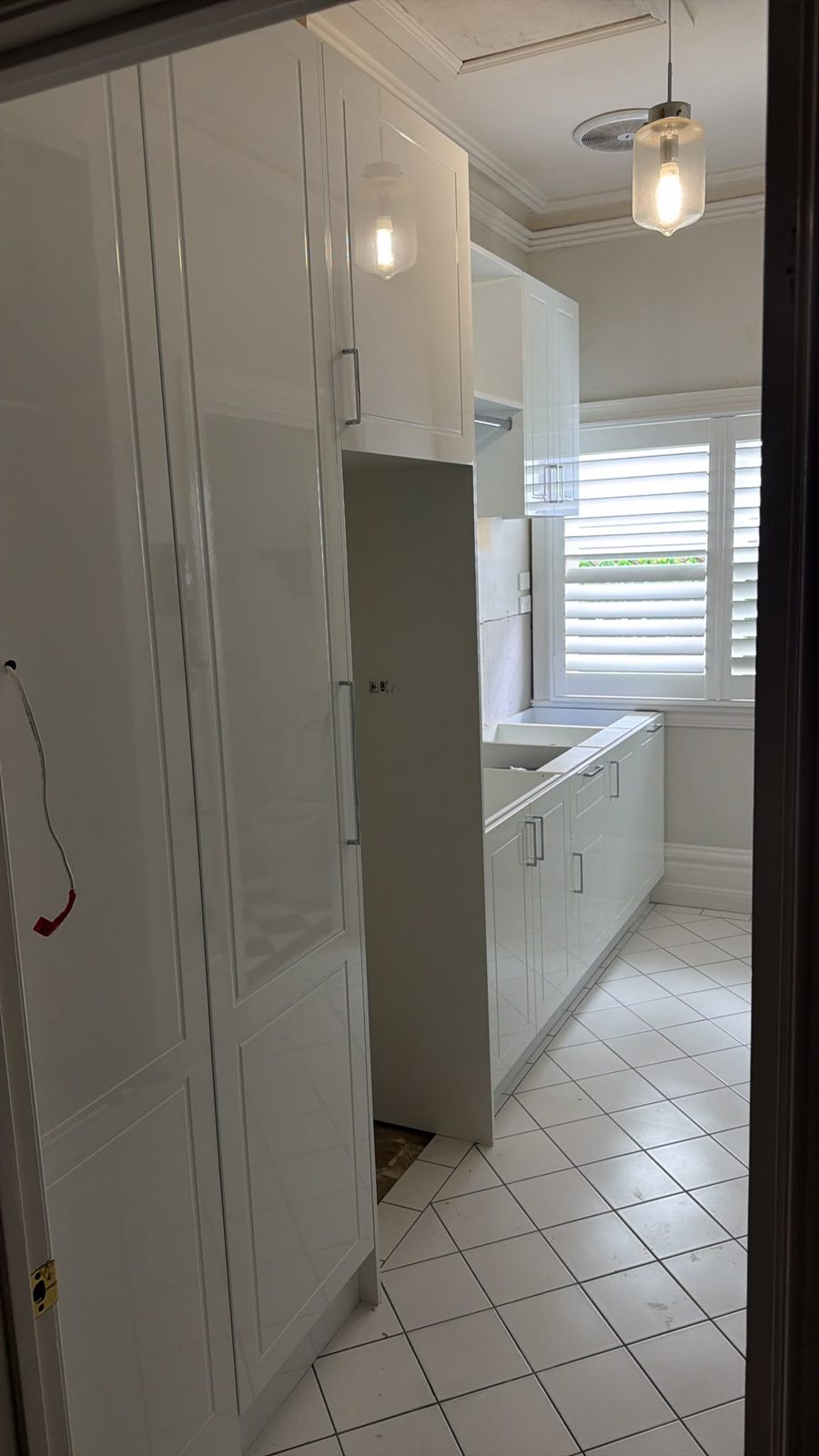 Laundry renovation at installation stage — cabinetry fitted, appliances and splashback tiles not yet installed, showing the full-height cabinet column and benchtop layout