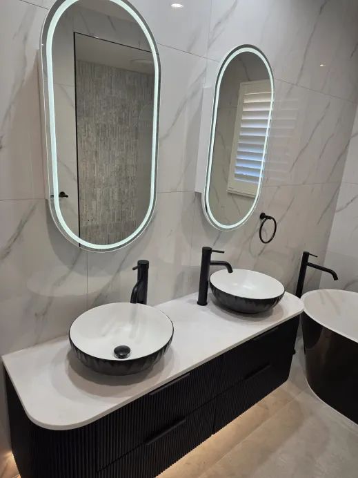 Double vanity with twin black vessel basins and LED oval mirrors