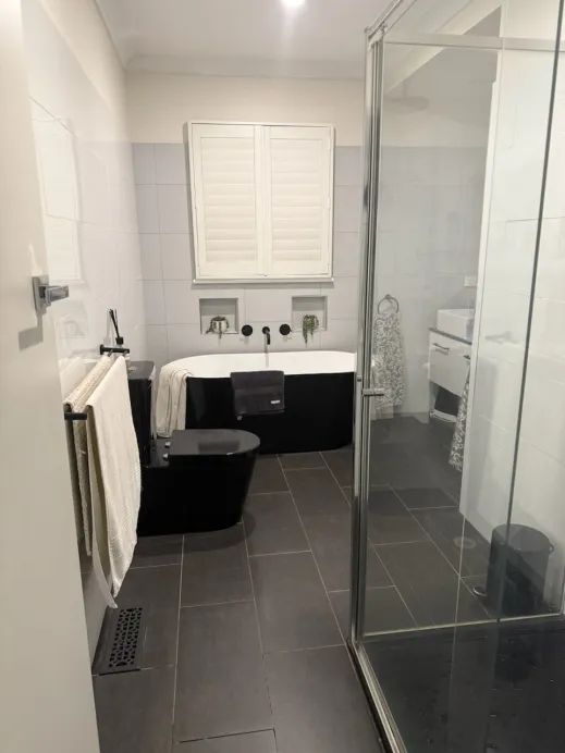 Existing Newcomb bathroom before renovation — black bath, dark floor tiles and partial wall tiling