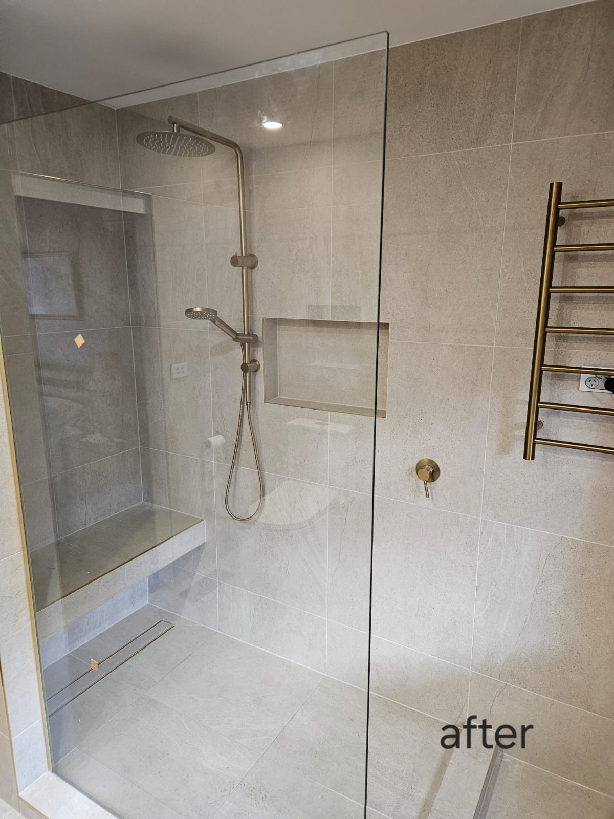 Shower detail with rainfall head, tiled niche, built-in seat, linear drain and brass towel rail